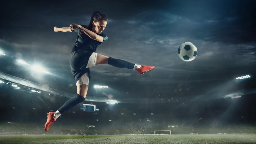 Football player leaping to kick ball in stadium