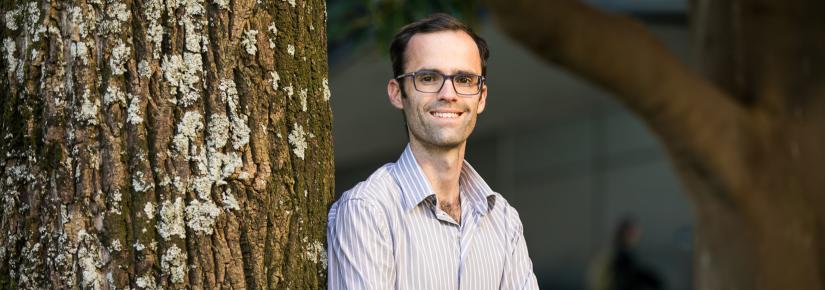 Associate Professor Harry Hobbs leans against a tree with his arms crossed.