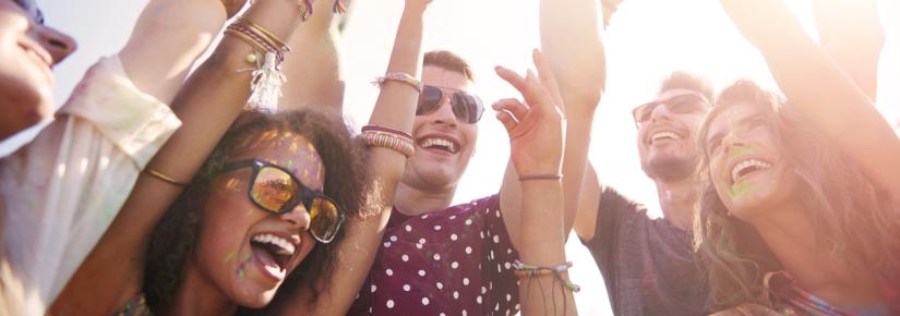 A group of people gathered at a festival with their hands in the air and looking excitedly in the distance.