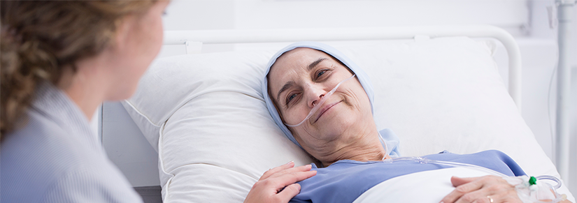 Senior woman with head scarf smiles at carer from hospital bed