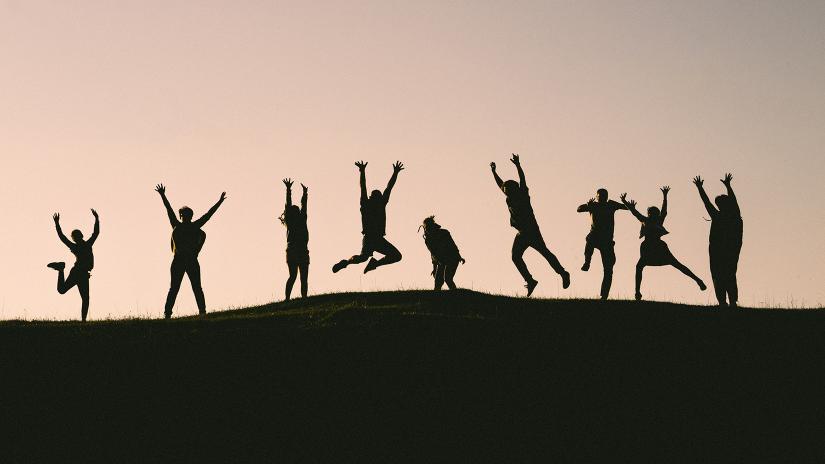 Group of people silhouetted jumping on a hilltop at dusk