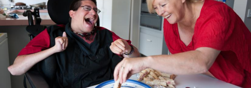 Man in a wheelchair laughing with a women at the dining table eating lunch.