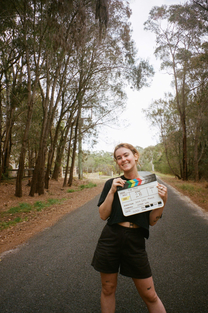 India smiles in a wooded area holding a clapper board