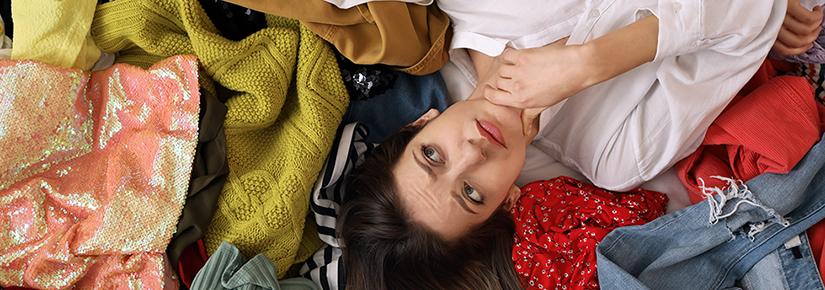 Stock picture of a young woman lying on pile of different clothes, top view. Fast fashion concept