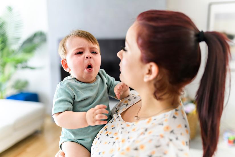 Stock picture of a coughing toddler in its mother's arms