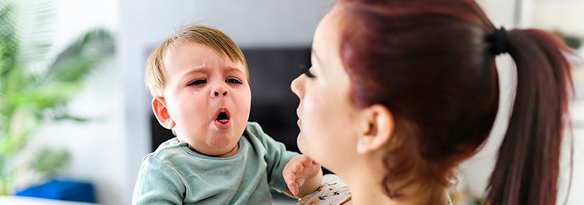 Stock picture of a coughing toddler in its mother's arms
