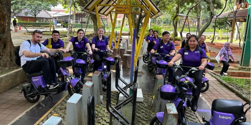 UTS Nursing students wearing purple polos pose outside for a photo in Jakarta, Indoesnia, sitting on purple motorised scooters.
