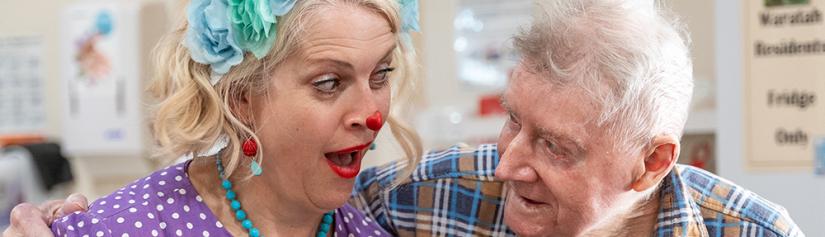 Laughter care clown and elderly man are looking at each other and smiling. 