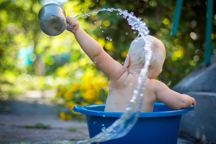Photo of the back of a toddler bathing in a plastic tub and tossing water