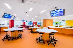 The Hive Superlab with colourful orange, red and yellow floors and walls, hexagonal white benches and large digital screens suspended from the ceiling