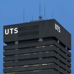 The top of the UTS Tower at night: a square concrete brutalist building with illuminated UTS signage