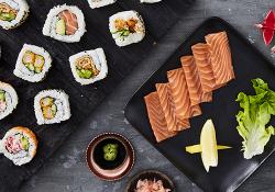 A tray of sushi rolls and sashimi, with bowls of pickled ginger and soy sauce