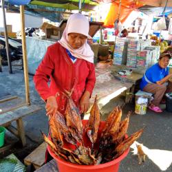 Woman in colourful head scarf with bucket of smoked fish at a street market