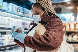 A woman in a protective mask looking at the ingredient label on a supermarket product