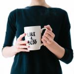 A woman holding a coffee mug that says 'Like A Boss'.