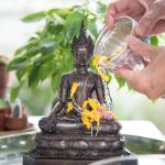 Hands pouring water over a statue of Buddha